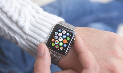 person in white sweater checking Apple Watch displaying colorful icons