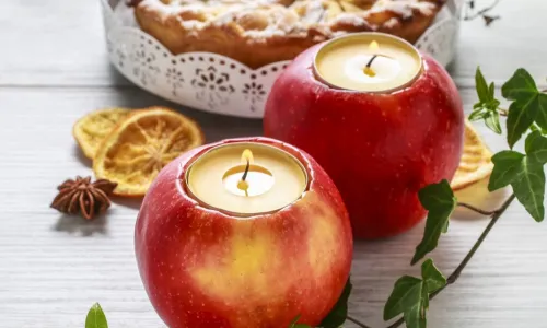 tea candles set into hollowed out apples sitting on a white wood table in front of a pie