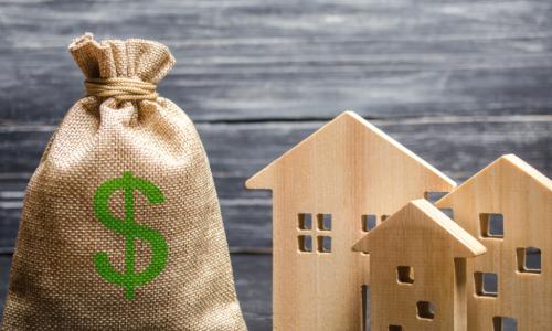 burlap bag with green dollar sign on it next to wooden houses
