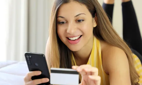 woman laying on a bed using credit card and smart phone