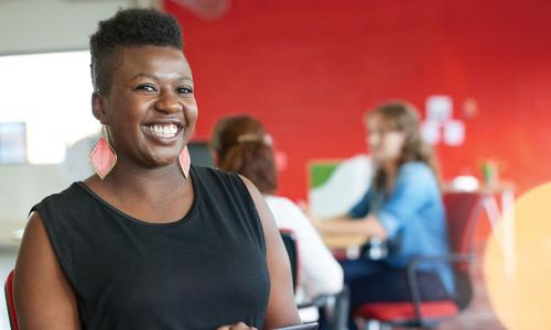 Smiling Black woman using tablet in busy workplace with bright red wall