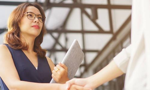 serious looking Asian businesswoman holding a portfolio shakes hands with vendor
