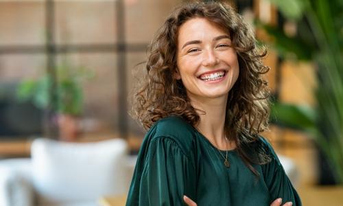 woman in green shirt with light brown curly hair smiling confidently at camera