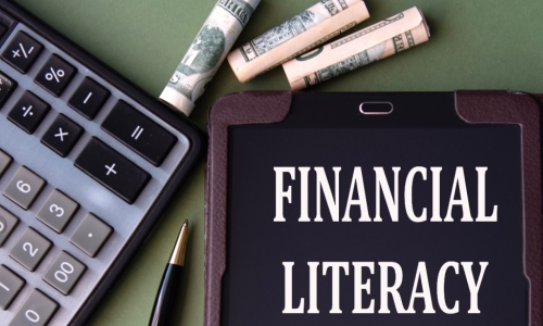 FINANCIAL LITERACY words appear on the screen of a tablet next to a calculator and banknotes