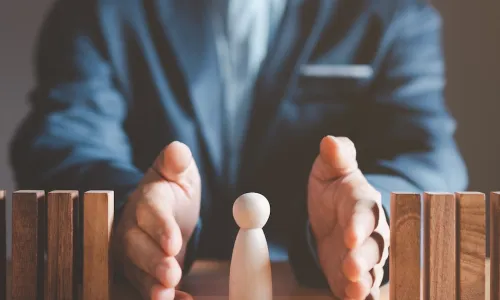 business leader protecting wooden person from falling dominoes