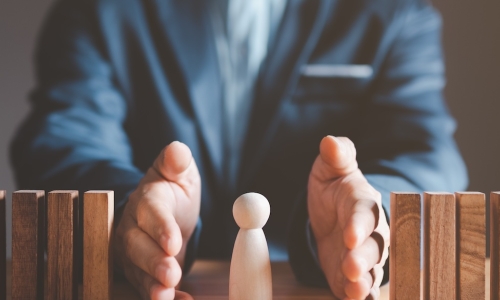 business leader protecting wooden person from falling dominoes