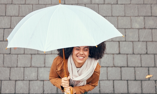 woman standing under an umbrella looking up smiling