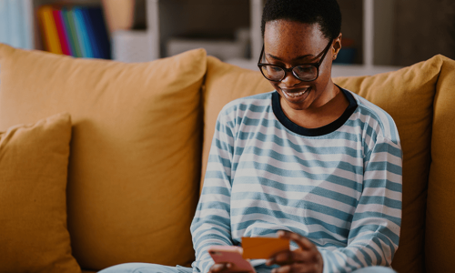 woman sitting on her couch looking at her smart phone and a business card