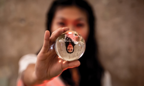 woman holding out glass ball with reflection of herself upside down within ball