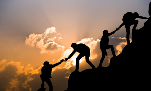 mountain climbers reach back to help the others up the climb