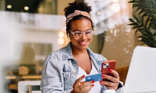 woman looking at her credit card and smart phone with big smile on her face