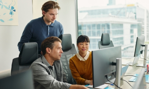 3 individuals looking at a desktop monitor