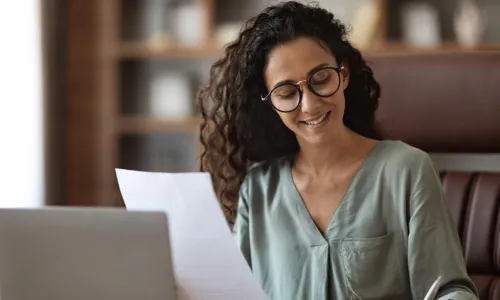 woman smiling writing while holding paper in other hand