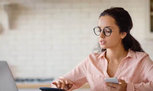 woman sitting in front of a laptop, calculator and smart phone