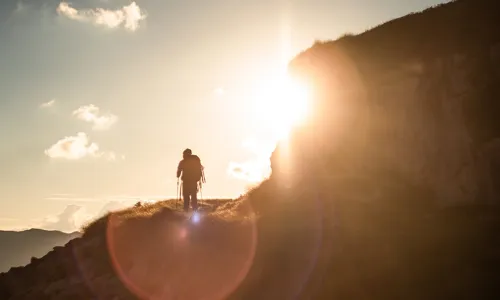man climbing mountain walking into the sun