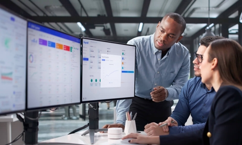 individuals looking at a 3 monitor set up while talking